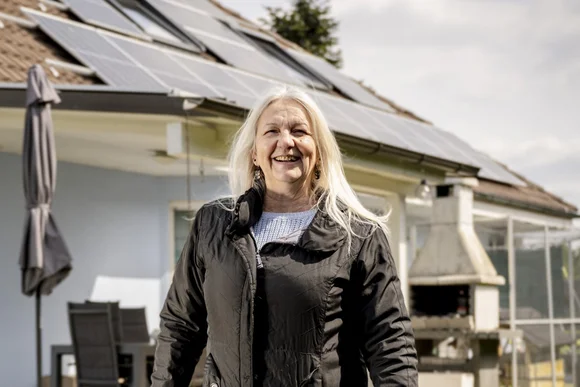 Lächelnde Person vor Haus mit Solarzellen