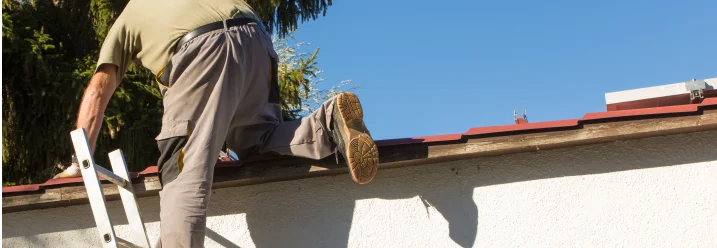 Eine Person klettert über eine Leiter auf ein Hausdach
