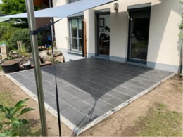 Gepflasterte Terrasse mit Sonnensegel an Haus