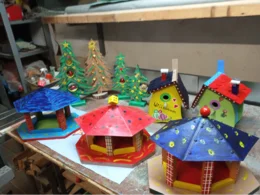 Bunte, handgefertigte Vogelhäuschen, Futterkrippen und Weihnachtsbäume aus Holz auf einer Werkbank.