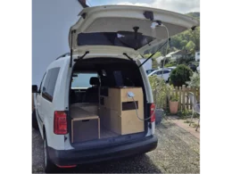 Ein weißer Van mit geöffnetem Kofferraum, der als Wohnmobil ausgebaut ist.