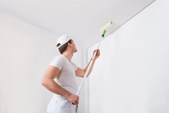 Person streicht Decke mit Farbrolle