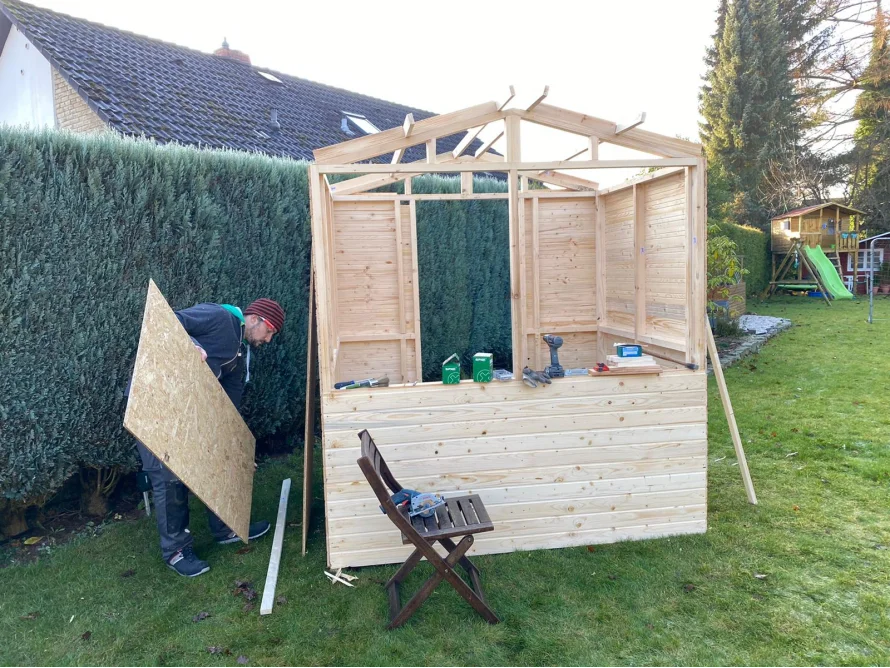 Person baut ein Gartenhaus aus Holz