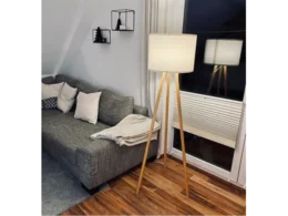 Eine Stehlampe mit Holzbeinen und weißem Lampenschirm.