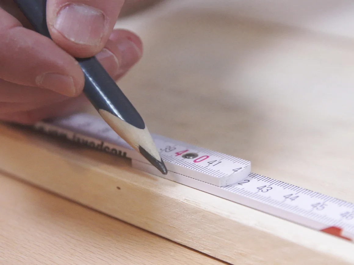 Person markiert Holz mit Bleistift und Zollstock