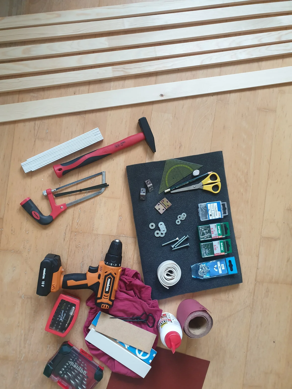Verschiedene Werkzeuge und Materialien für ein Holz-Heimwerkerprojekt auf dem Boden ausgelegt.