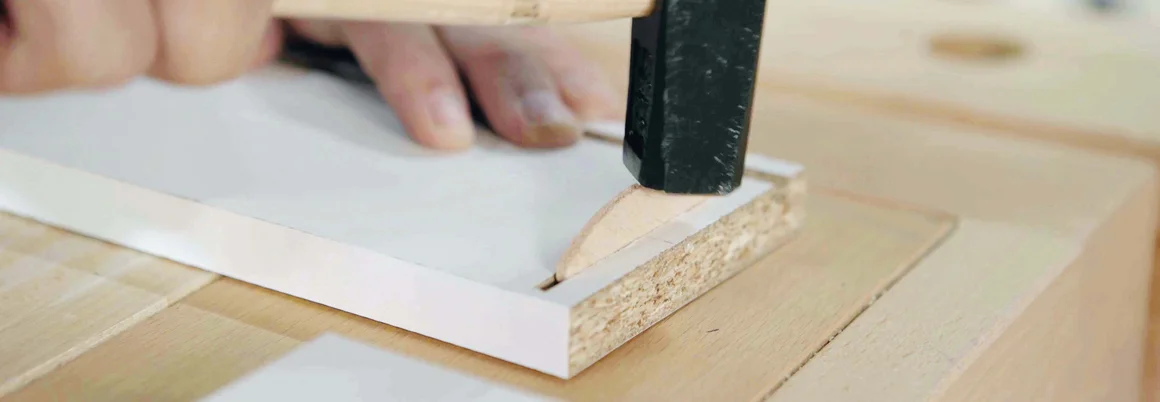 Hand hämmert Holzdübel in Holzbrett
