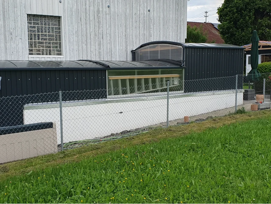 Eine schwarze Überdachung für einen Kellerabgang mit transparentem Dach und Fenster.