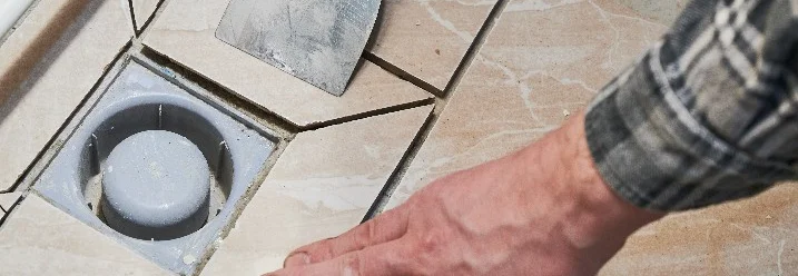 Hand verlegt Fliesen um einen Duschabfluss.