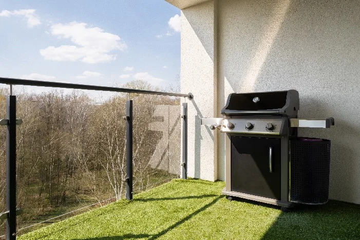 Ein Gasgrill auf einem Balkon mit Kunstrasen.