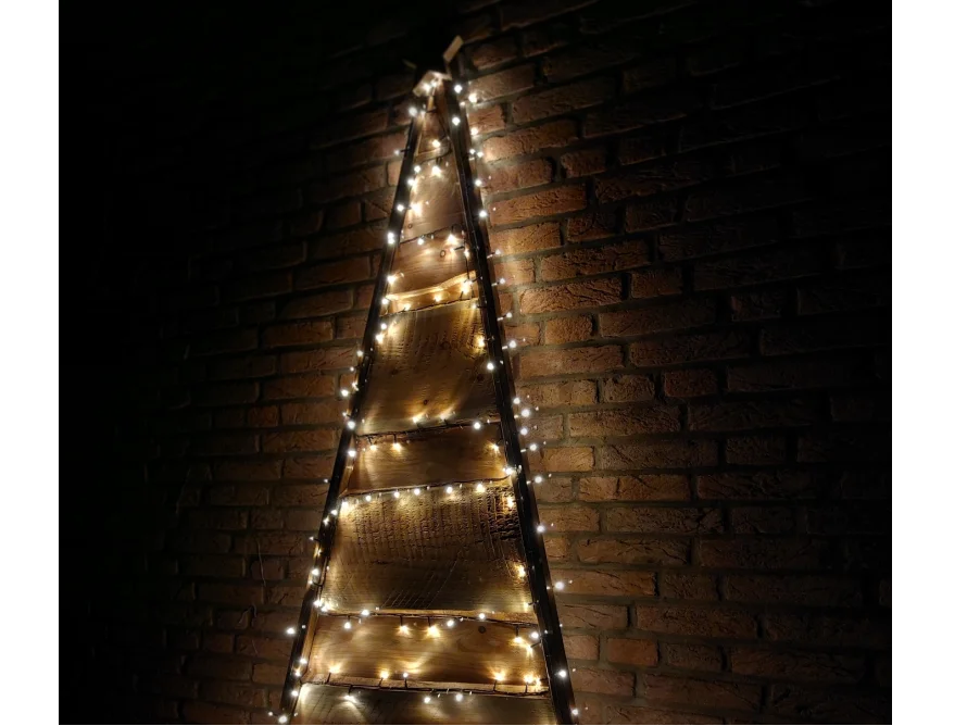 Rustikaler Holz-Weihnachtsbaum mit Lichterkette an Backsteinwand