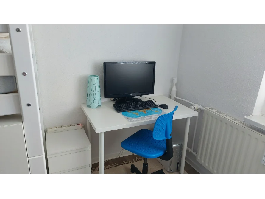 Ein weißer Schreibtisch mit einem Computer und einem blauen Stuhl in einer Ecke.