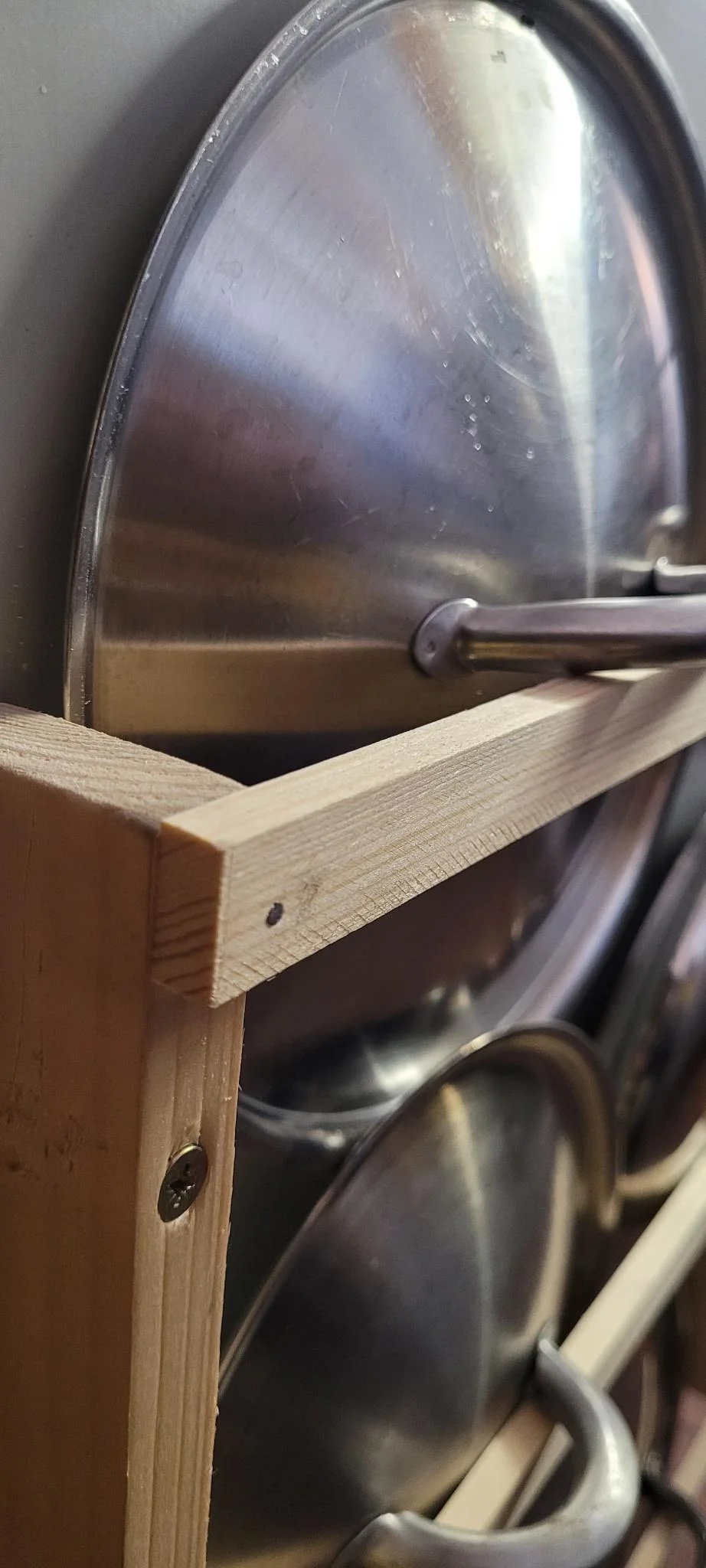 Nahaufnahme von Topfdeckeln aus Edelstahl in einem Holzregal.
