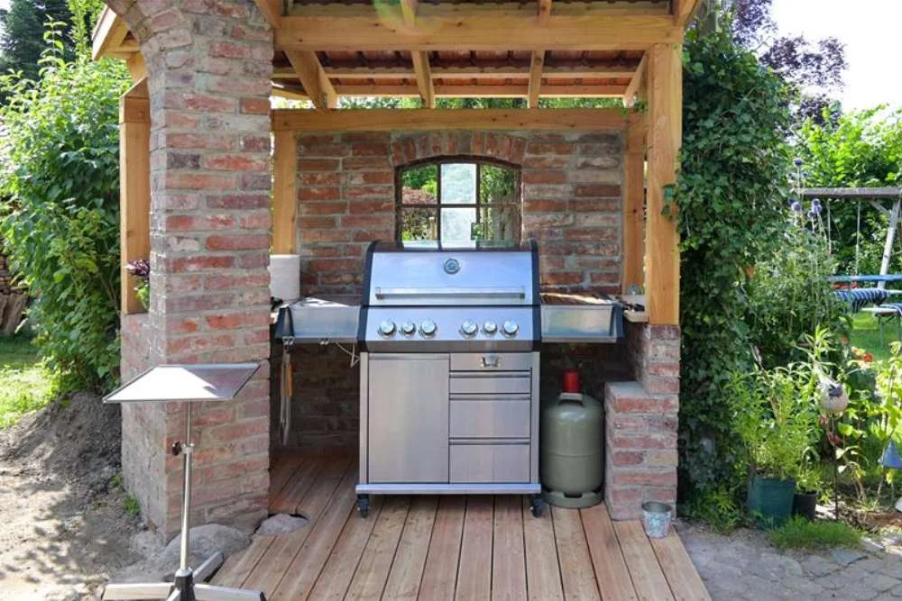 Moderner Stahlgasgrill in einem Unterstand aus alten Ziegeln und Holzkonzept-