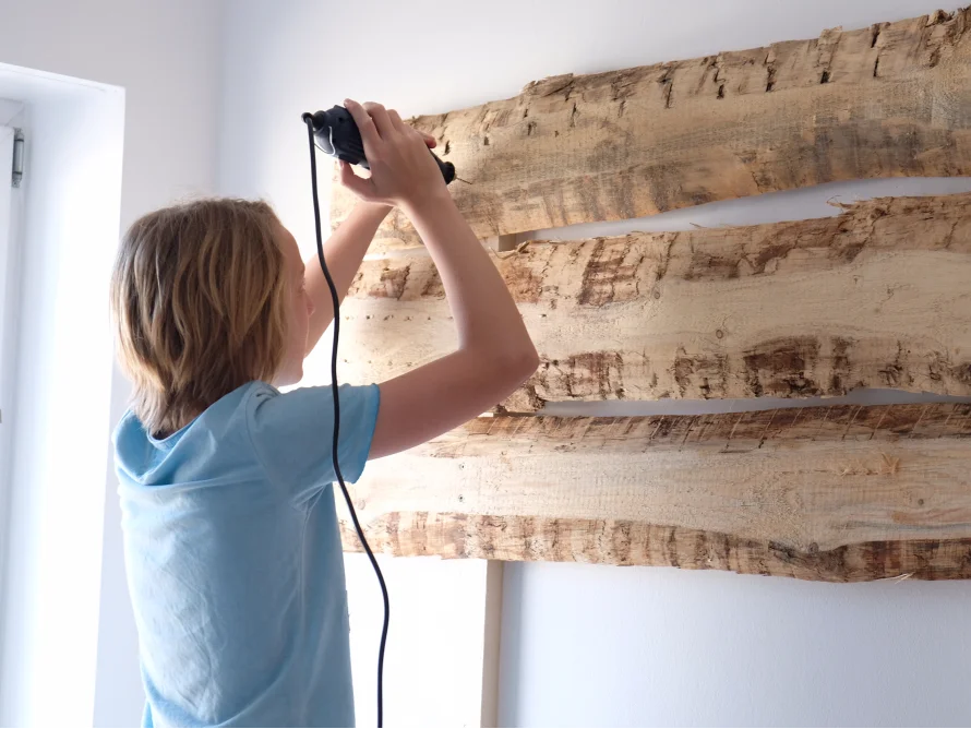 Kind befestigt Holzbretter an Wand