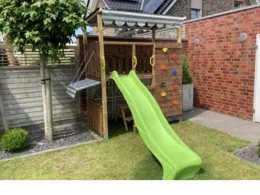 Ein Holzturm mit Rutsche und Kletterwand im Garten.