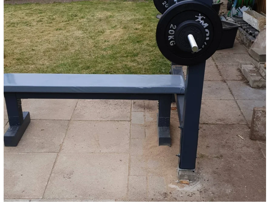 Eine schwarze Hantelbank mit einer Gewichtsscheibe steht auf einer Terrasse.