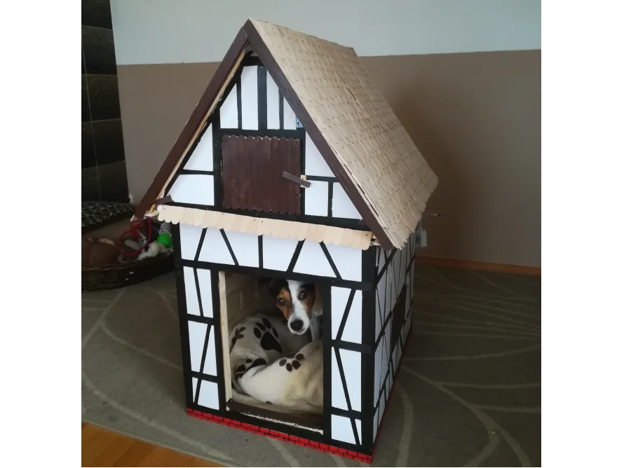 Ein Hund schaut aus einer Hundehütte in Form eines Fachwerkhauses