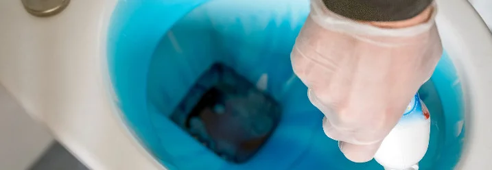 Hand mit Reiniger und blauer Flüssigkeit in einer Toilette