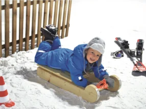 Kind liegt auf einem Holzschlitten im Schnee