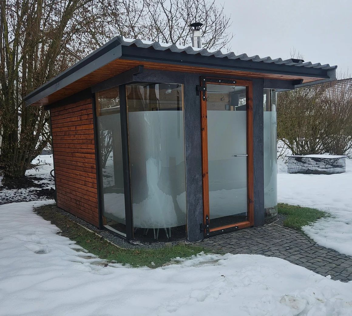 Eine moderne Außensauna mit Glasfront im verschneiten Garten.