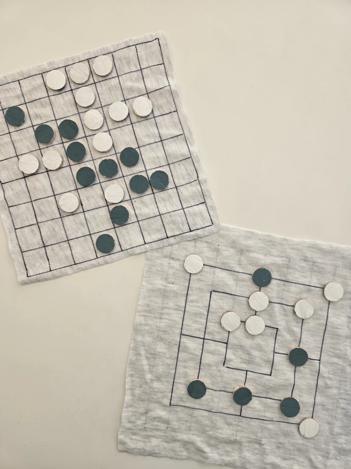 Zwei selbstgemachte Brettspiele aus Stoff mit weißen und grünen Spielsteinen.