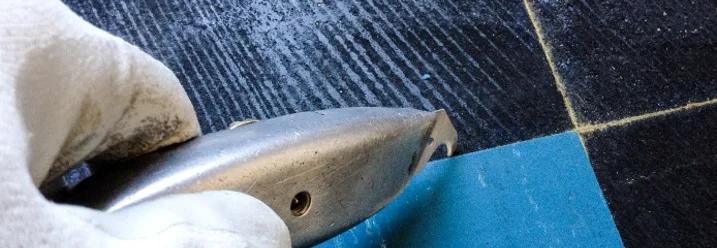 Hand mit Teppichmesser entfernt Fliesenkleber