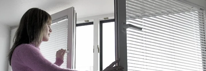 Person öffnet Fenster mit Jalousie