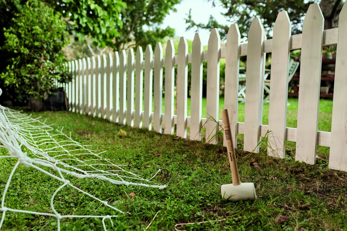Weißer Gartenzaun und Fußballnetz auf einer Wiese.