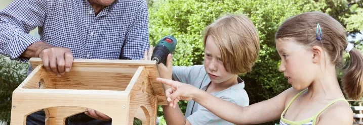Eine Person baut mit Kindern ein Vogelhaus