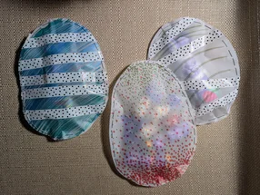 Drei selbstgebastelte Ostereier aus Transparentpapier, verziert mit gepunktetem Klebeband und zusammengeheftet.