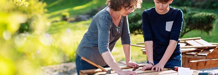 Zwei Personen bauen ein Holzgestell mit einem Hammer zusammen.
