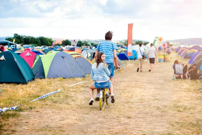 Zwei Personen fahren mit dem Fahrrad über einen Campingplatz.