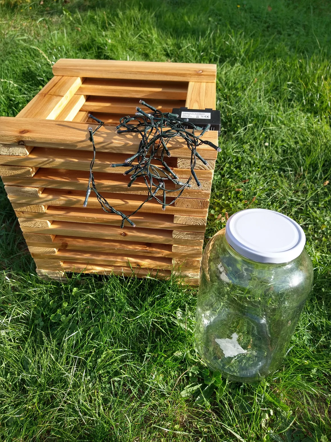 Holzgestell, Lichterkette und Glas auf einer Wiese.