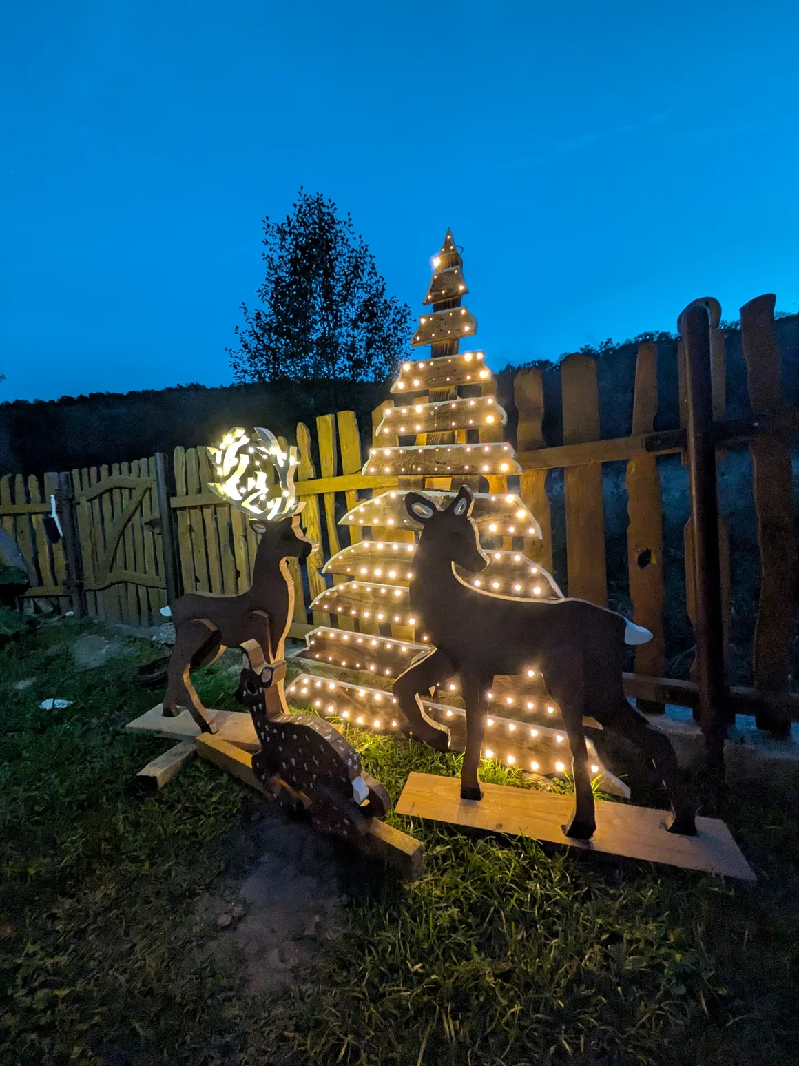 Beleuchtete Weihnachtsdekoration aus Holz in Form von Rehen und einem Baum.