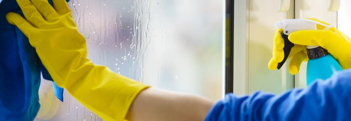 Person reinigt Fenster mit Lappen und Sprühflasche