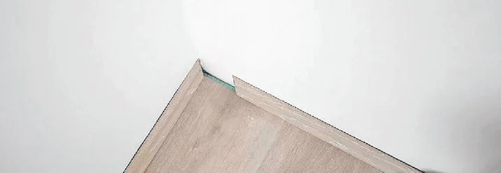 Person verlegt Laminat in einer Ecke.