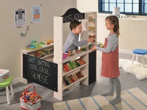 Zwei Kinder spielen mit einem hölzernen Kaufladen.