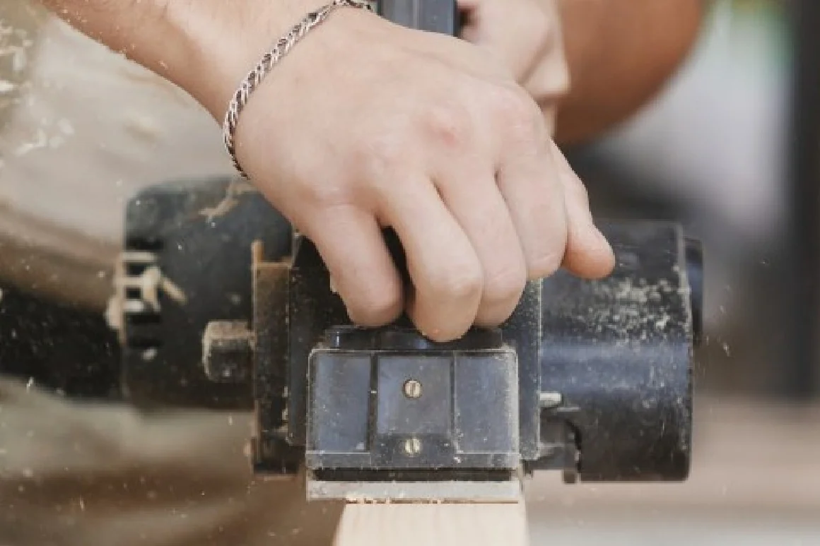 Hand führt Elektrohobel über Holz