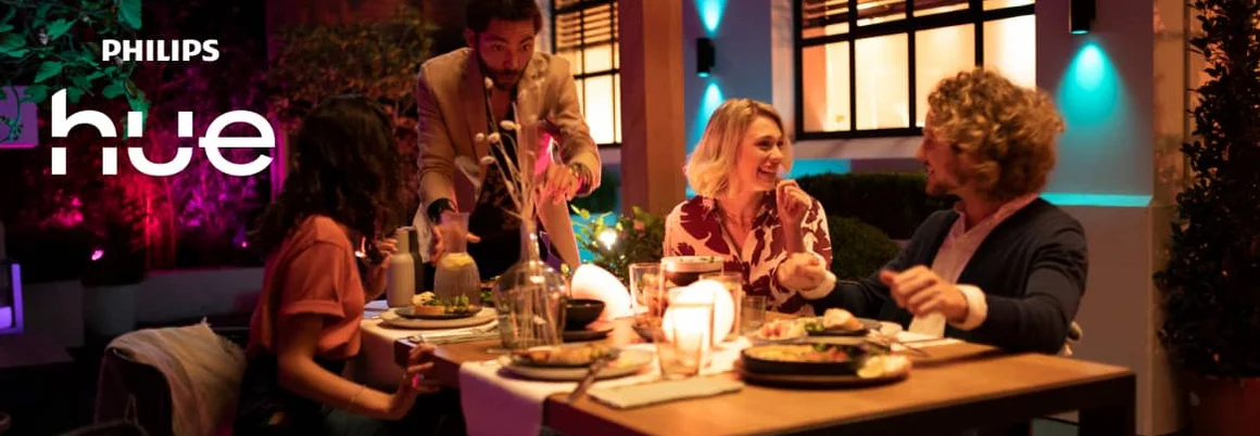 Mehrere Menschen sitzen an einem Tisch in einem mit Philips Hue ausgeleuchteten Wohnzimmer