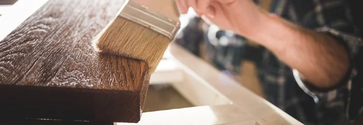 Person beizt Holz mit Pinsel
