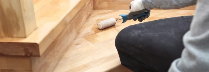 Person ölt Holztreppe mit Hilfe einer Rolle