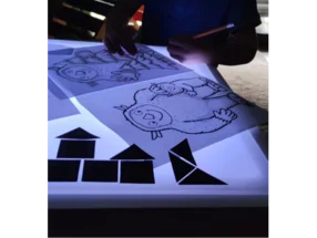 Person zeichnet ein Monster auf einem Leuchttisch mit Bleistift nach.