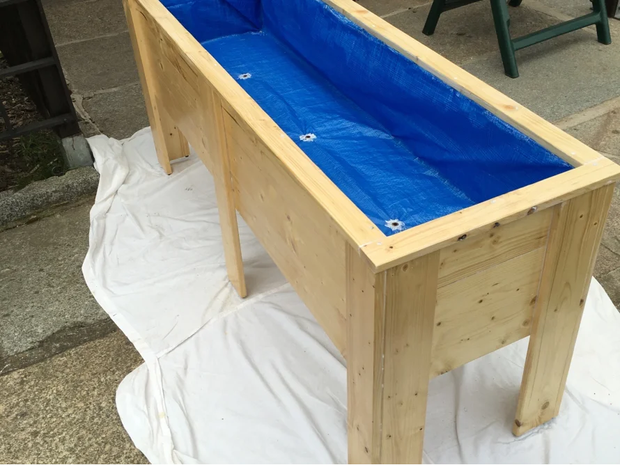 Hochbeet aus hellem Holz mit blauer Folie ausgelegt