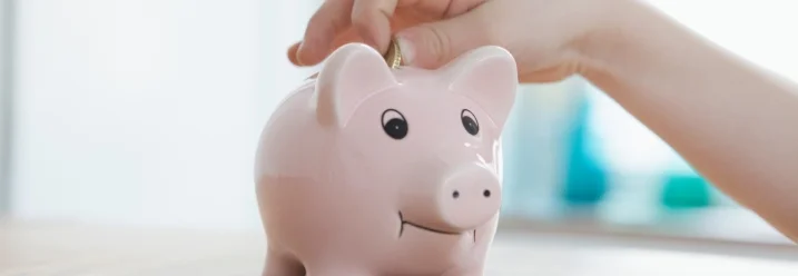 Ein Kind steckt eine Münze in ein rosa Sparschwein.
