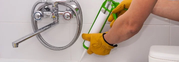 Person verwendet Dichtmittel an Badewannenrand