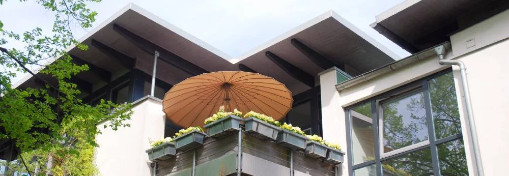 Balkon mit Sonnenschirm und bepflanzten Hochbeeten.