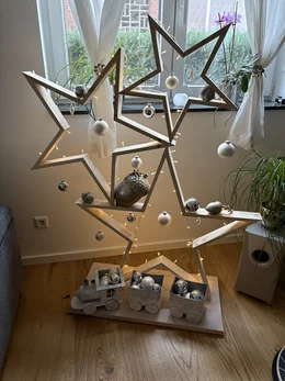 Moderner Weihnachtsbaum aus Holzsternen, dekoriert mit Kugeln und einer Lichterkette.