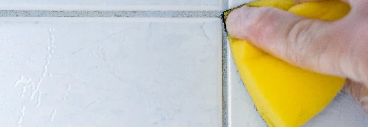 Hand reinigt Fliesenfugen mit Schwamm