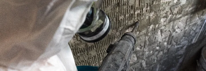Person mit Atemschutzmaske entfernt Fliesenkleber mit Bohrhammer
